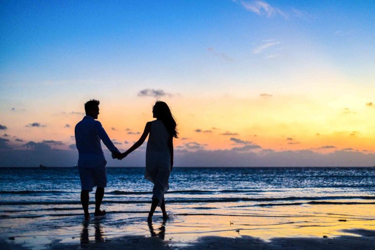 man and woman holding hands on the beach at sunset